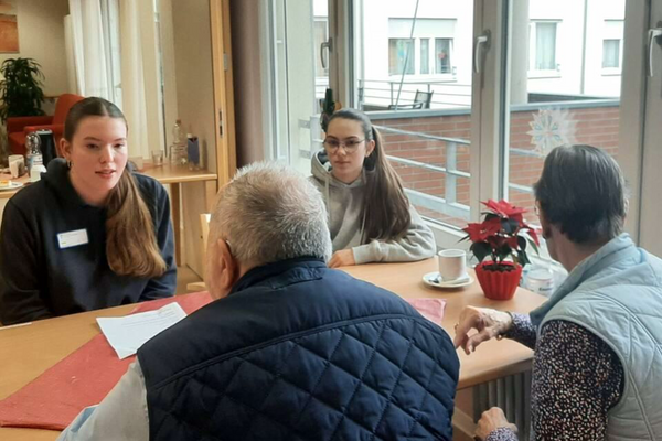 Zwei junge Leute sitzen am Tisch mit einer Seniorin und einem Senior